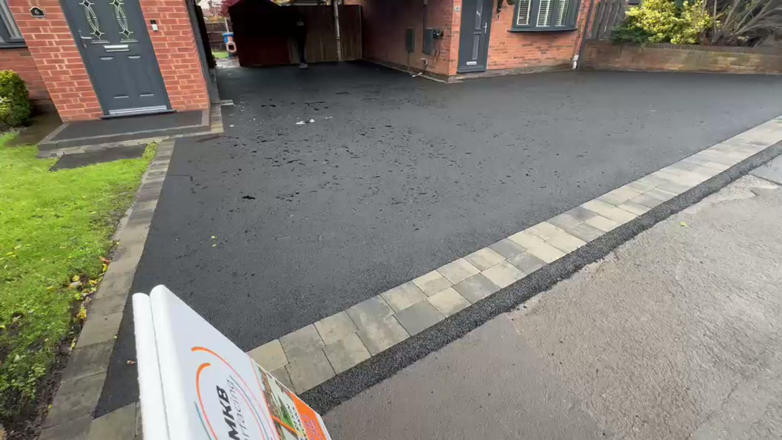 Black tarmac driveway edged with decorative block paving at a brick house