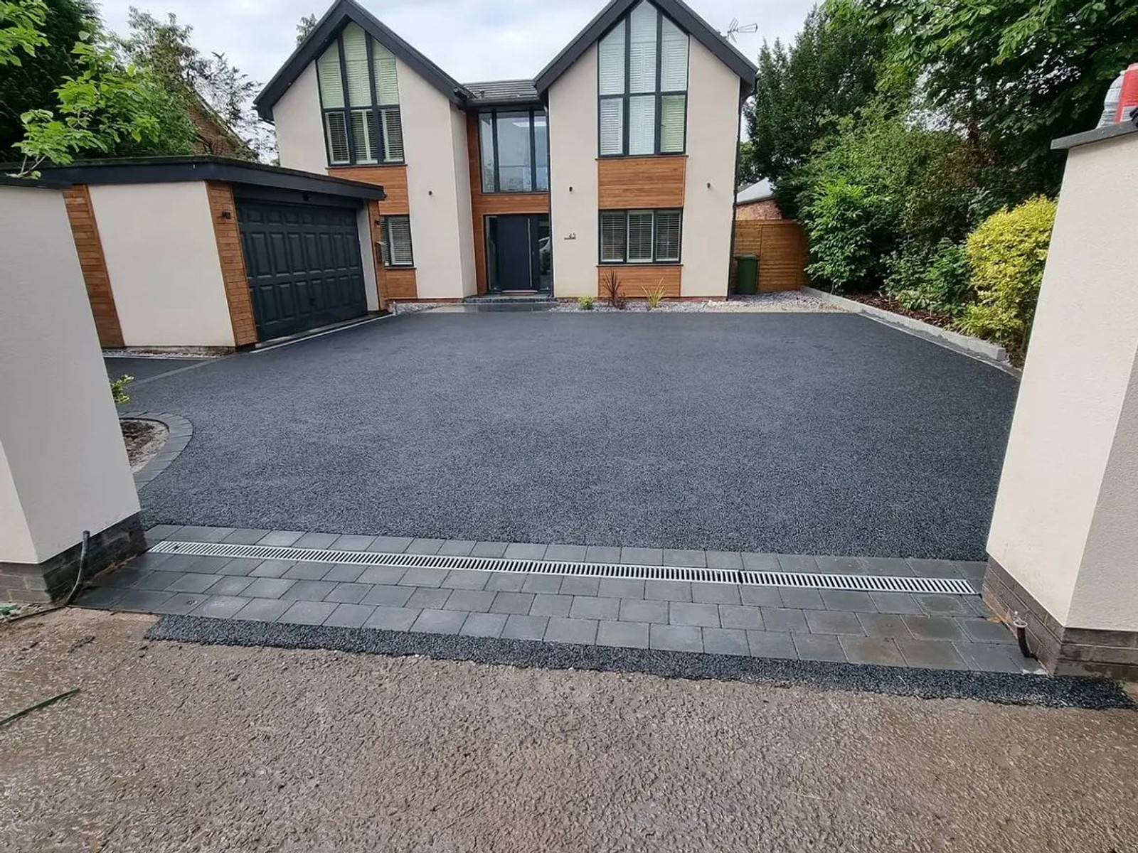 Finished dark charcoal driveway with block paving drainage channel in front of a modern home