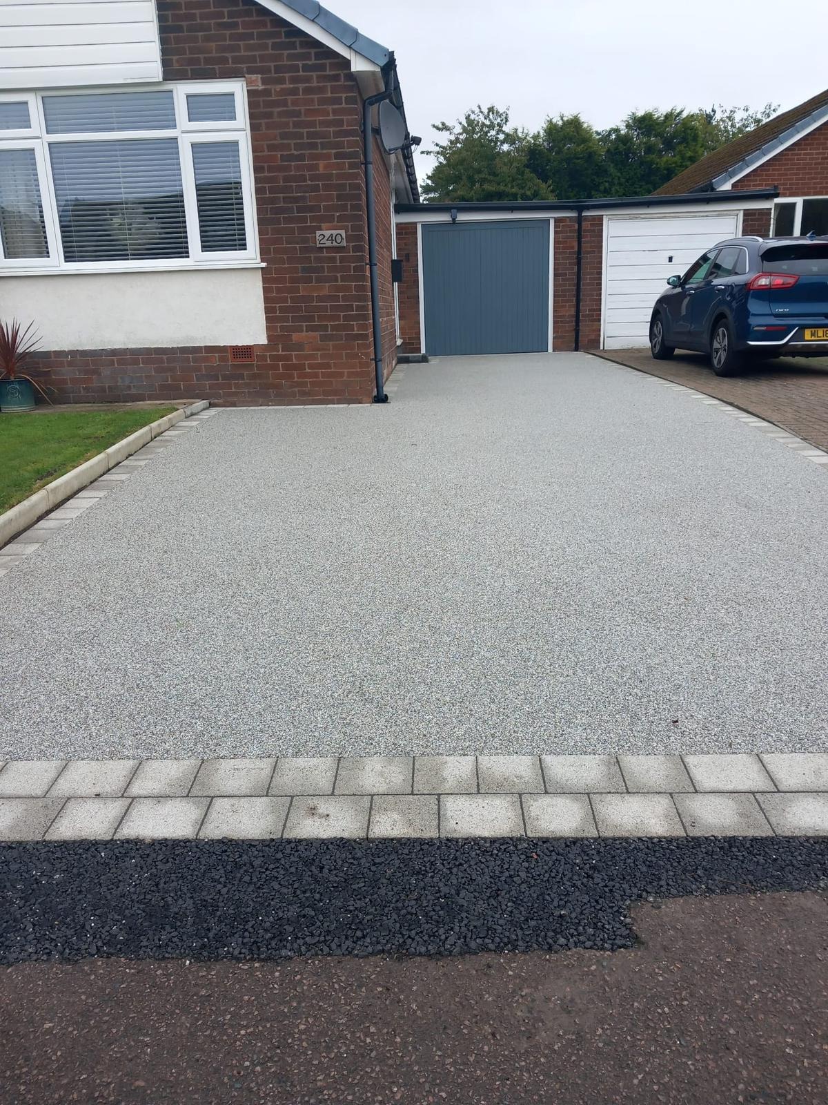 Light grey resin driveway to a blue garage door with block border