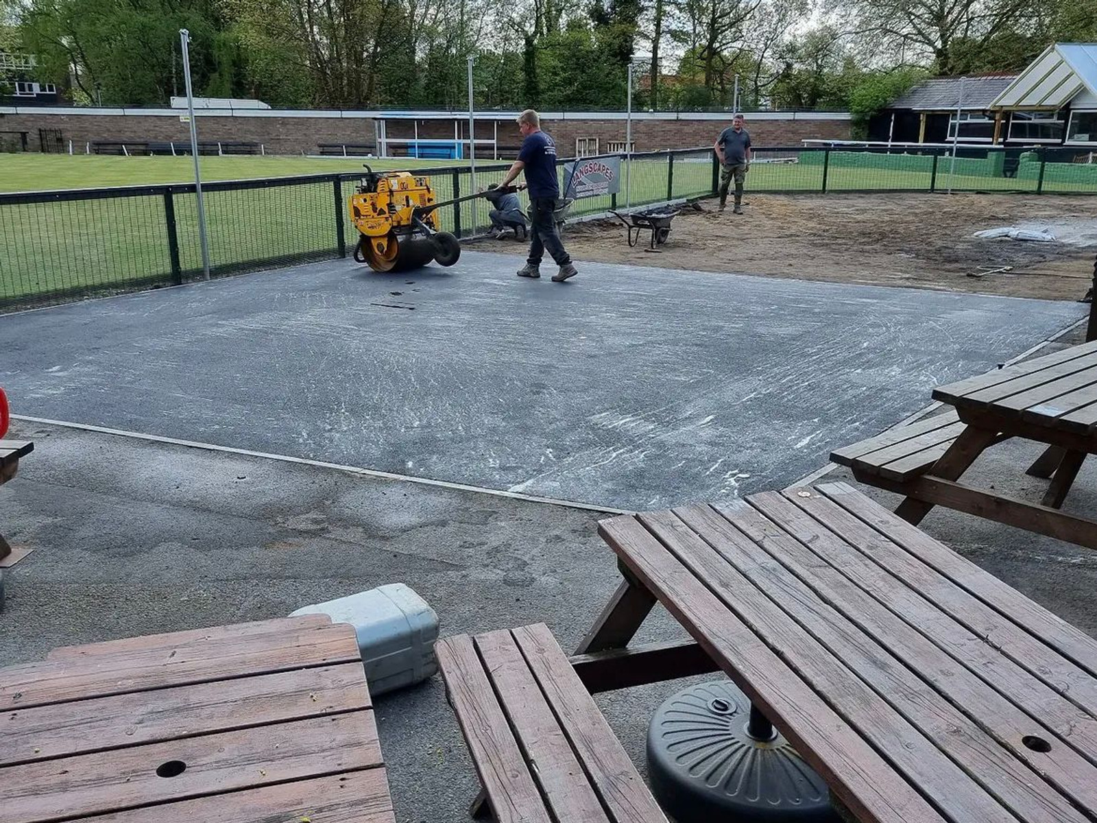 Surfacing team compacting newly laid asphalt with a roller on a commercial site